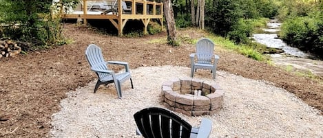 Een camping met een vuurkuil, twee Adirondack stoelen en een overdekte ruimte met een koepelconstructie.