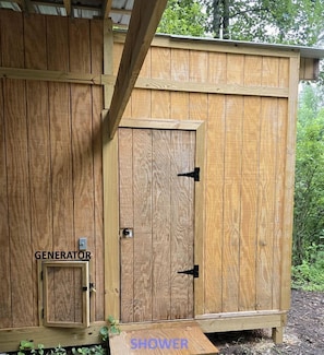 A wooden shed with a door labeled 'GENERATOR' and a smaller door labeled 'SHOWER.'