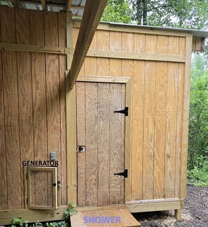 A wooden shed with a door labeled 'GENERATOR' and a smaller door labeled 'SHOWER.' - Geodome on Creek, Great Getaway, WIFI & Hot Shower near Boone, NC (Purlear)