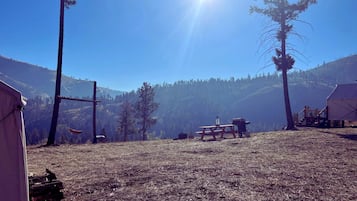 A campsite with tents, a picnic table, and a clear view of a forested mountain range.