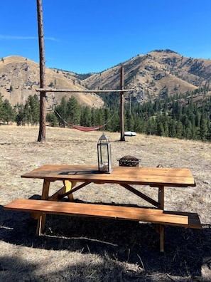 A picnic table with a lantern and a fire pit in a natural setting with mountains in the background.