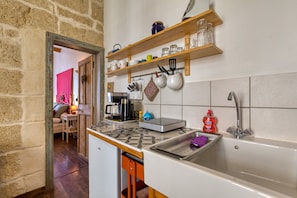 A kitchen with a built-in dishwasher, a sink, and a coffee maker. There are shelves above the sink holding various kitchen items.