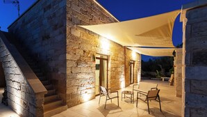En bygning i sten med trappe, udendørs siddeområde og en overdækket terrasse.