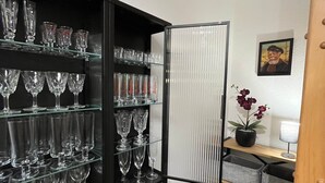 A compact room with a black shelving unit filled with wine glasses, a potted plant, and a framed picture on the wall. - Lüttje Deichvilla Backbord (Wurster Nordseeküste)