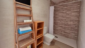 A bathroom with a wooden shelf unit, a toilet, and a shower area with a patterned wall. - Connect with yourself in a space of peace and tranquility. (Arbo)