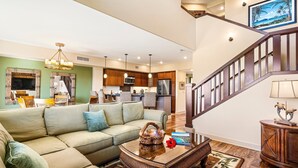A spacious living room with a large sectional sofa, a coffee table, and a staircase leading to the upper floor. - Amazing Ocean, Golf & Sunset Views Great Location Private Bbq! - Vrkcv (Waikoloa)