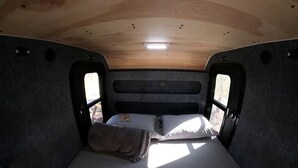 Interior compacto de una autocaravana con una cama individual, una mesita y una ventana.