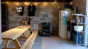 Una cocina con una mesa de madera, un refrigerador y repisas con diversos artículos.