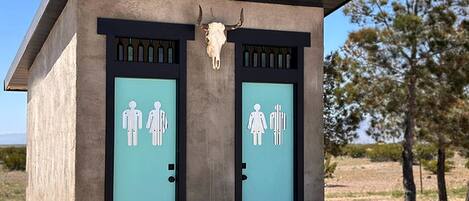 Un edificio pequeño con dos puertas, cada una señalada con símbolos de género, y un cráneo de toro montado sobre las puertas.