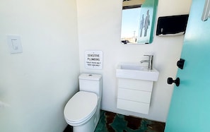 A small bathroom with a toilet, a sink, and a sign indicating sensitive plumbing.