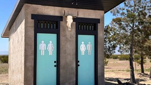 A small building with two doors, each marked with gender symbols, and a bull skull mounted above the doors.