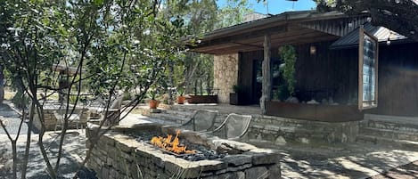 Un foyer en pierre avec des sièges, entouré d’arbres et agrémenté d’un patio couvert.