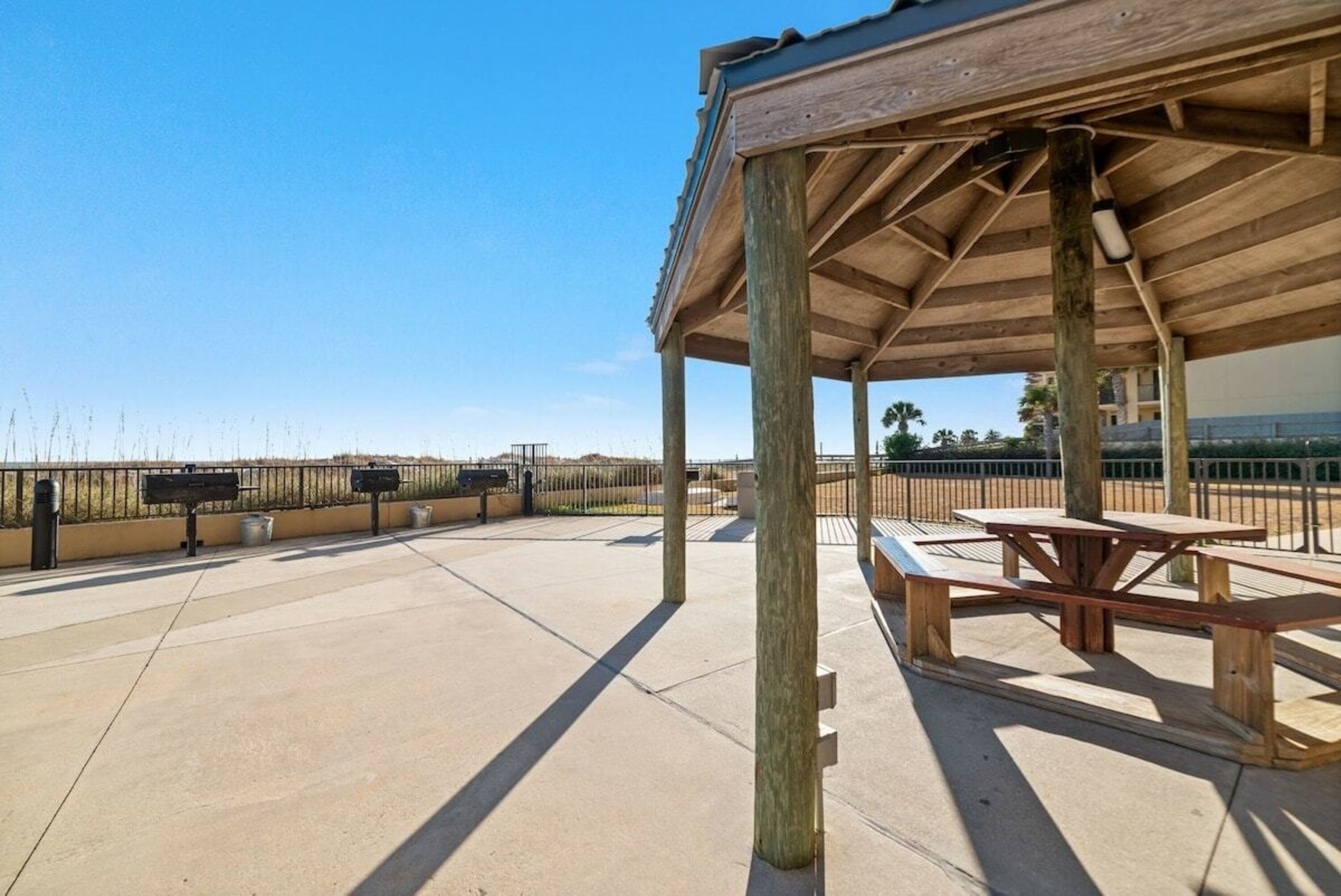 An outdoor patio area with a wooden pergola, picnic tables, and a view of the beach.