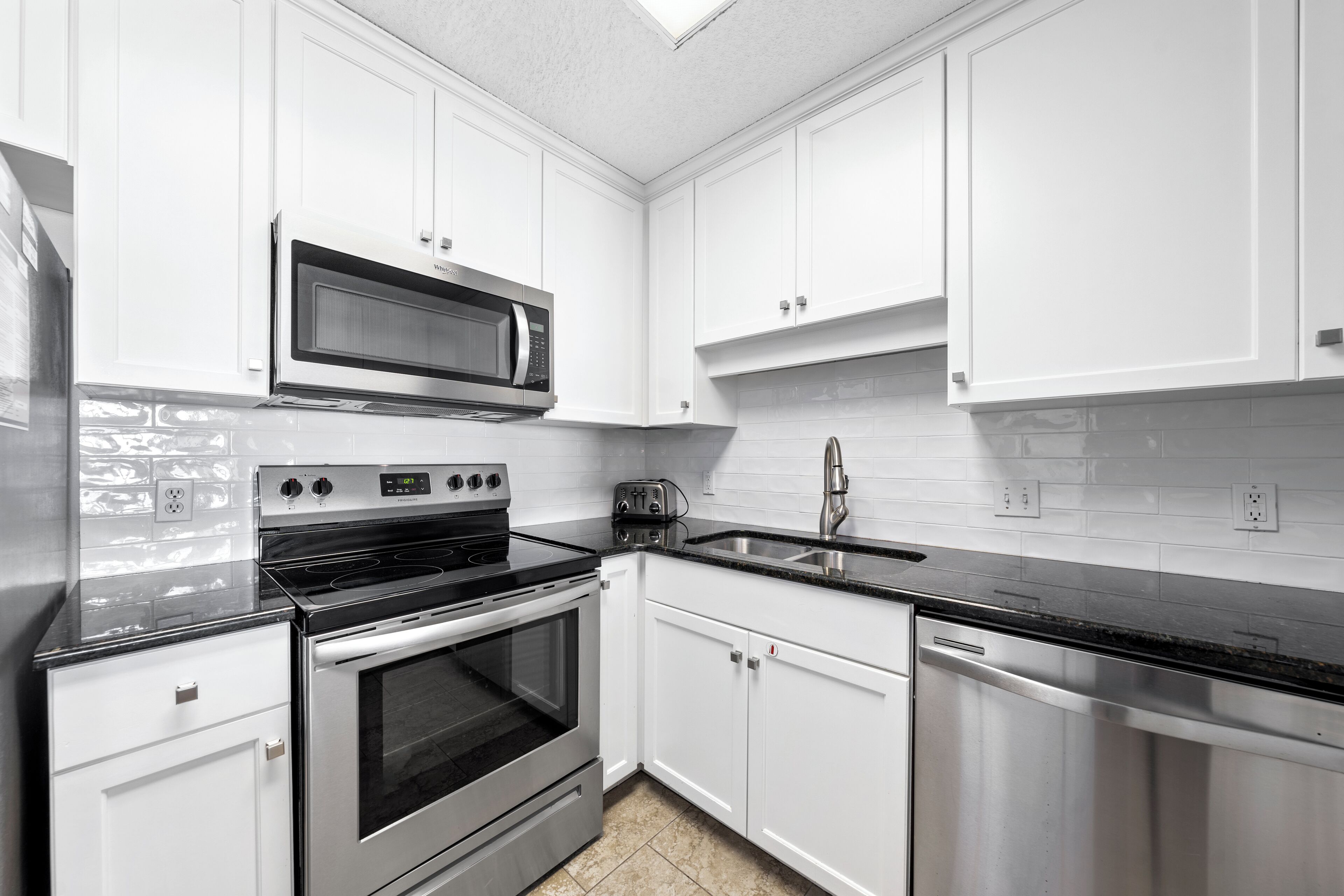 A modern kitchen with white cabinets, stainless steel appliances, and a black countertop.