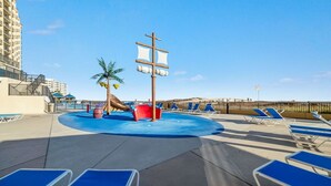 Ein Poolbereich mit blauen Liegestühlen, einer Palme und einer Piraten-Schiffs-Dekoration.