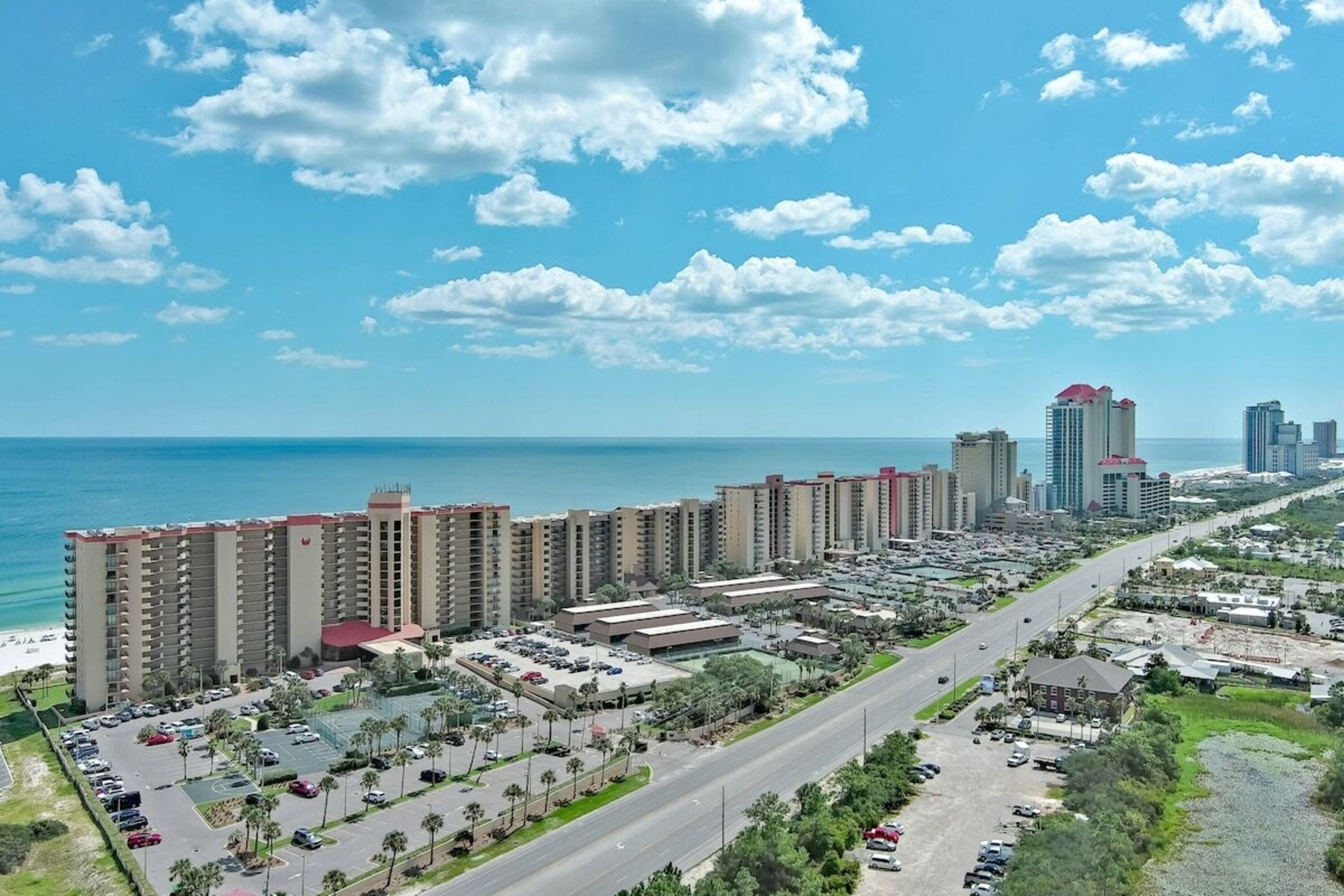A high-rise hotel with multiple floors, a parking lot, and a view of the ocean.