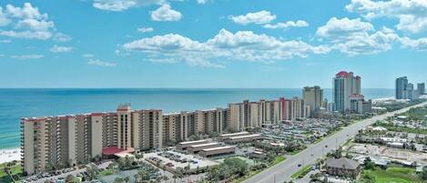A high-rise hotel with multiple floors, a parking lot, and a view of the ocean.