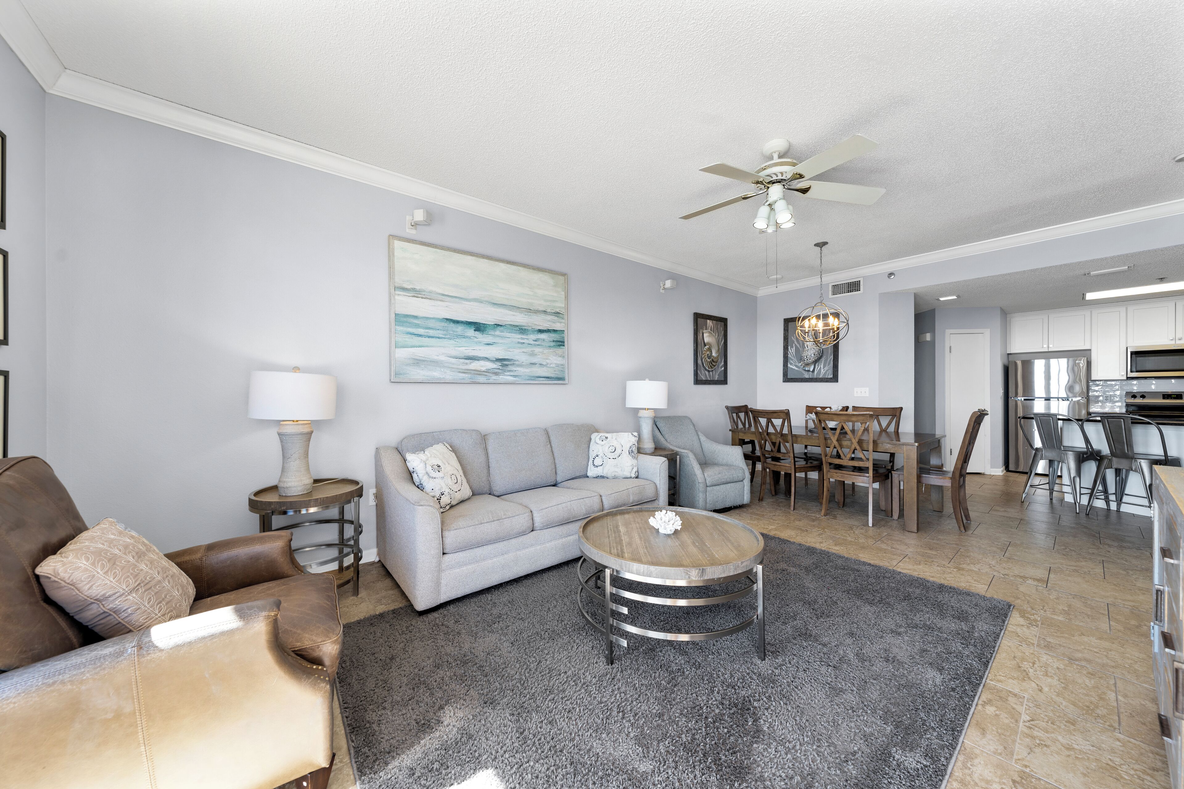 A modern living room with a grey sofa, a round coffee table, and a dining area with a chandelier.