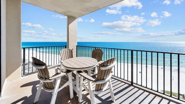 Ein Balkon mit Tisch und Stühlen mit Blick auf einen Strand.