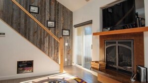 Un salon moderne avec un escalier en bois, une cheminée et un grand téléviseur fixé au mur.
