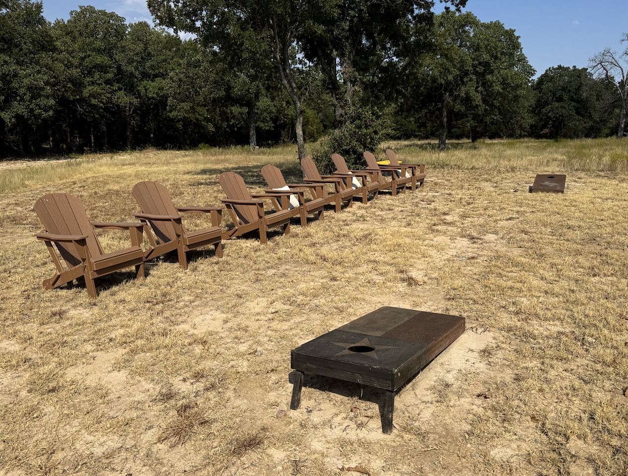 Una hilera de sillas de madera y una mesa con forma de estrella en un campo cubierto de césped, con árboles al fondo.