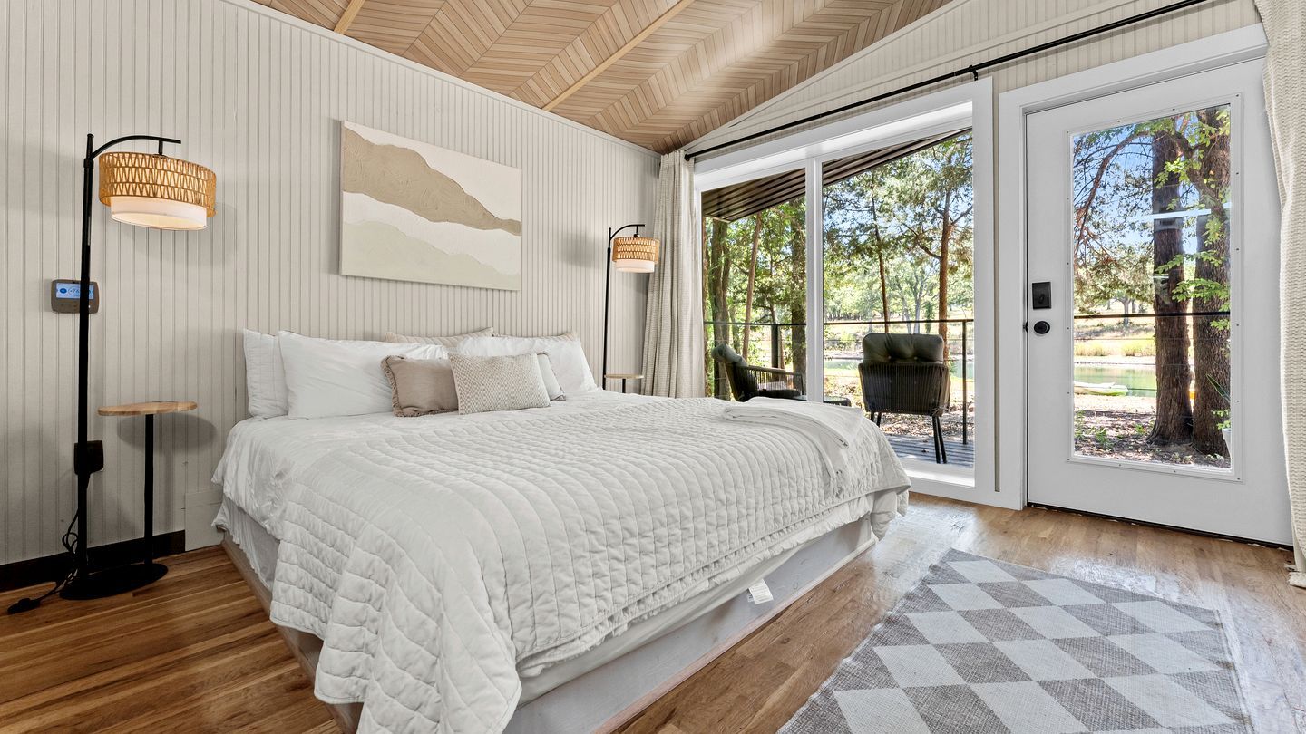 Un dormitorio con una cama grande, una lámpara de pie y vistas al exterior a través de un ventanal corredera.