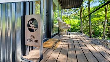 Een houten terras met een metalen hekwerk, een bord met een vogel logo en een stoel.