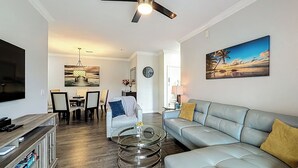 Ett modernt vardagsrum med en grå soffa, ett soffbord i glas och en takfläkt.