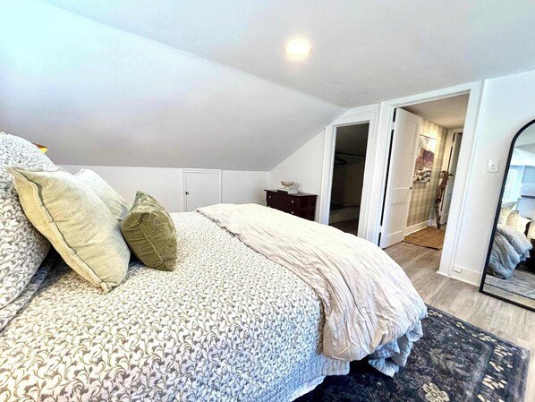 A bedroom with a bed, a dresser, a mirror, and a door leading to a bathroom.
