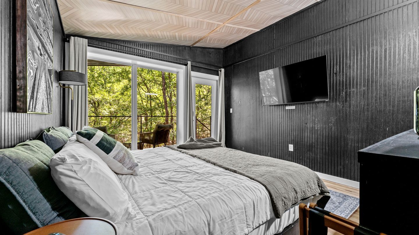 A bedroom with a bed, a TV, and a window with a view of trees.
