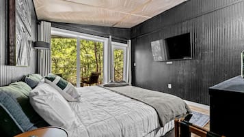 A bedroom with a bed, a TV, and a window with a view of trees.