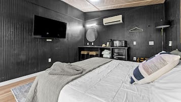 A bedroom with a bed, a television, a mirror, a microwave, and a hanging light fixture.