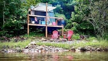 Una cabaña con terraza, dos sillas Adirondack y un pequeño hogar para fuego.