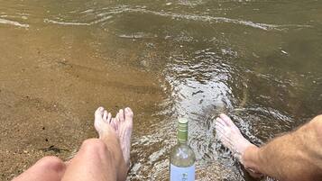 A bottle of Seaglass wine on a sandy beach with clear water.
