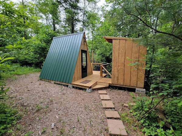 A small wooden cabin with a green roof and a wooden door, surrounded by dense forest. - Cool A-Frame on Creek in Purlear, North Carolina (Purlear)