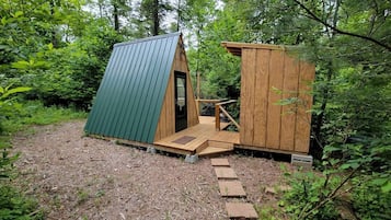 Eine kleine Holzhütte mit einem grünen Dach und einer Holztür, umgeben von dichtem Wald.