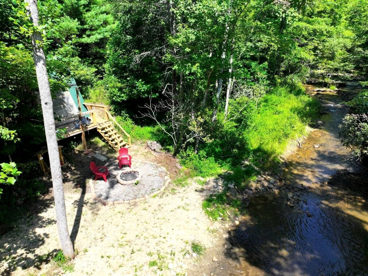 A forested area with a wooden deck, a fire pit, and a small stream.
