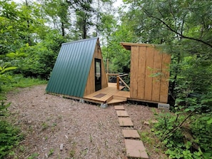 A small wooden cabin with a green roof and a wooden door, surrounded by dense forest.