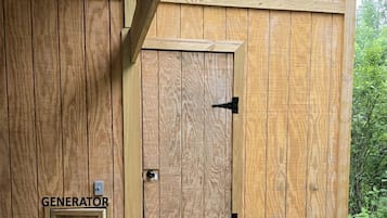 Un abri en bois avec une porte portant l’inscription « GÉNÉRATEUR » et une porte plus petite portant l’inscription « DOUCHE ».