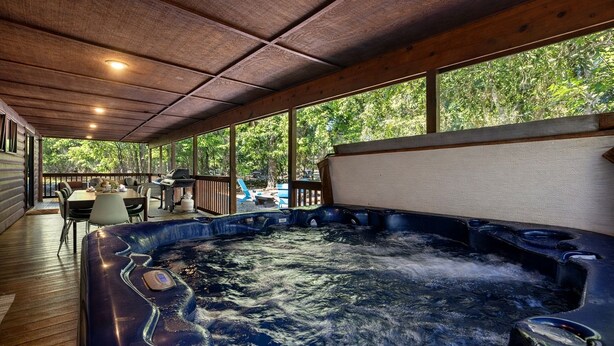 A hot tub in a covered outdoor area with a wooden deck, a table, and chairs. - Charming Cabin with Hot Tub Near Casino & State Park in Hochatown, Oklahoma (Broken Bow)