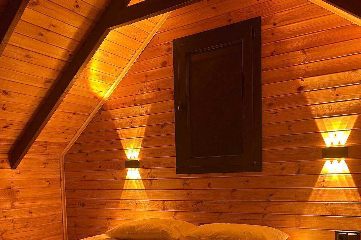 A cozy wooden room with a bed, sloped ceiling, and wall-mounted lights.