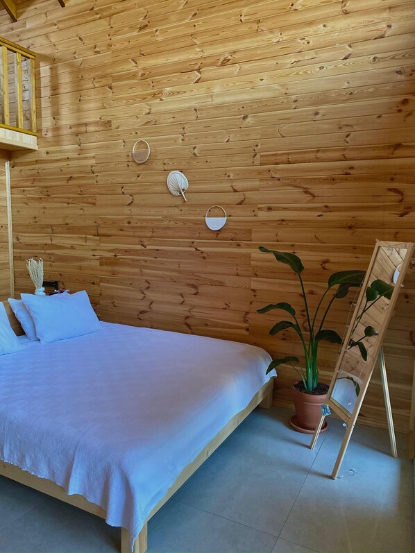 A wooden-paneled room with a bed, pillows, a potted plant, and a wall-mounted shelf. - Meşe Bungalov (Yalova)