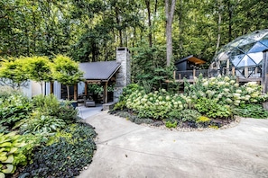 A modern house with a stone chimney, a covered patio, and a garden with various plants.