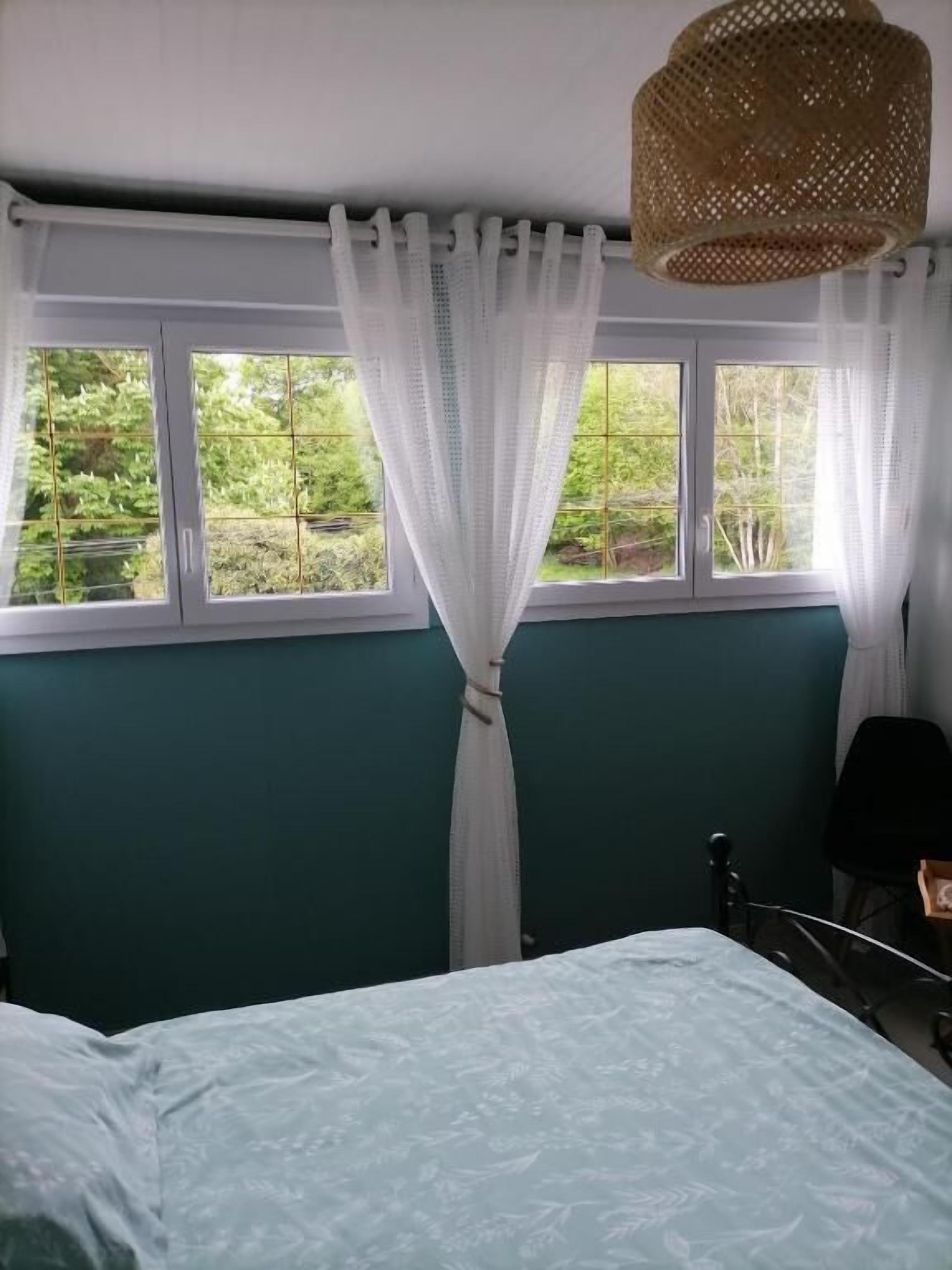 A bedroom with a bed, a window with a view of greenery, and a hanging light fixture.