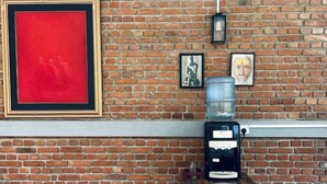 A dining area with a brick wall, a large red painting, a water dispenser, and a coffee machine. - Ko Lake -Eagle Nest r5 (Ahangama)