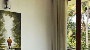A hotel room with a bed, a ceiling fan, a painting of a person walking in a forest, and a view of palm trees through a window. - Ko Lake -Eagle Nest r5 (Ahangama)