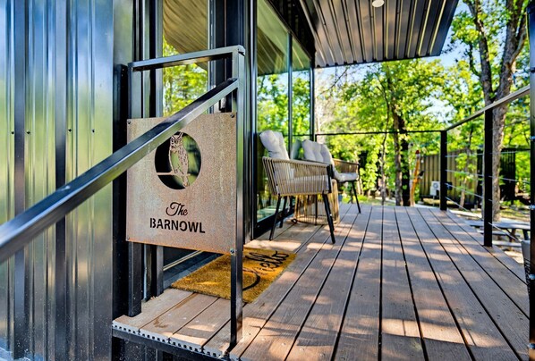 A wooden deck with outdoor seating, a sign reading 'The Barnowl,' and a glass door.