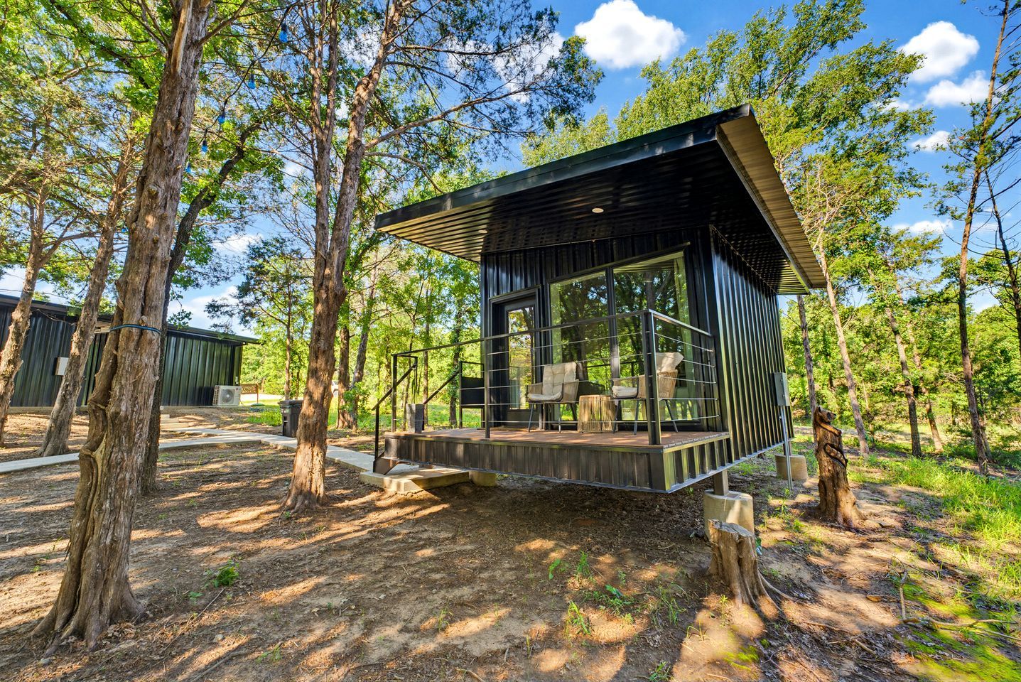 A modern cabin with a deck, surrounded by trees.