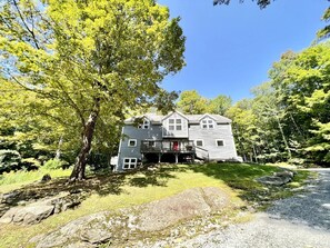 A two-story house with a balcony, surrounded by trees and a gravel driveway. - Secluded Cottage with Stunning Sights in Winhall, Vermont (Winhall)