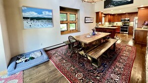 A spacious kitchen with wooden cabinets, a dining area with a bench, and a large rug. - Secluded Cottage with Stunning Sights in Winhall, Vermont (Winhall)